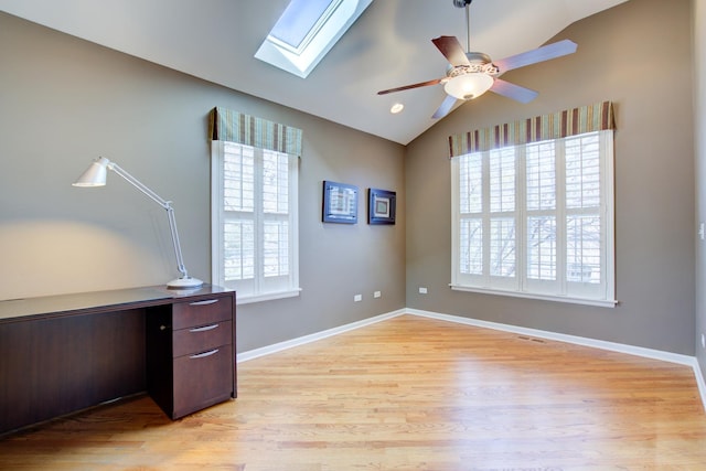 office with baseboards, vaulted ceiling with skylight, ceiling fan, and light wood finished floors