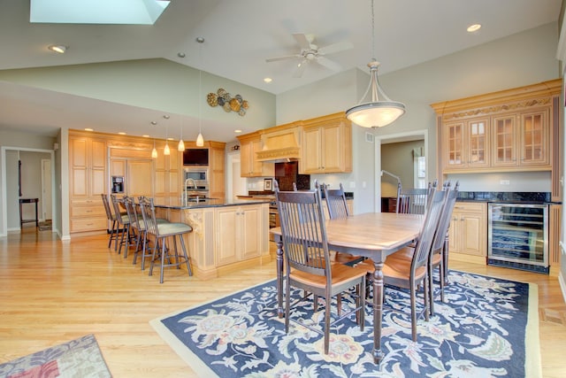 dining area with beverage cooler, light wood finished floors, high vaulted ceiling, a skylight, and ceiling fan