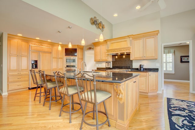 kitchen featuring light brown cabinets, a breakfast bar, custom exhaust hood, ceiling fan, and built in appliances