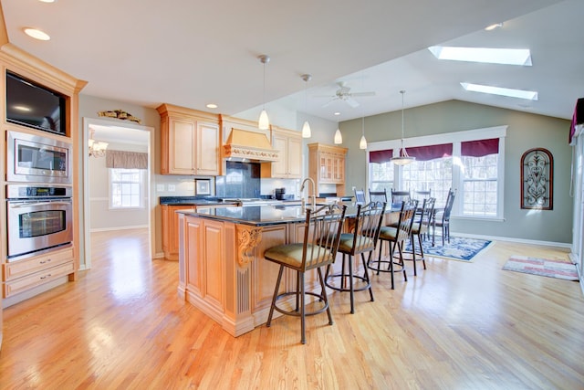 kitchen featuring lofted ceiling with skylight, a breakfast bar, appliances with stainless steel finishes, light wood-style floors, and custom exhaust hood