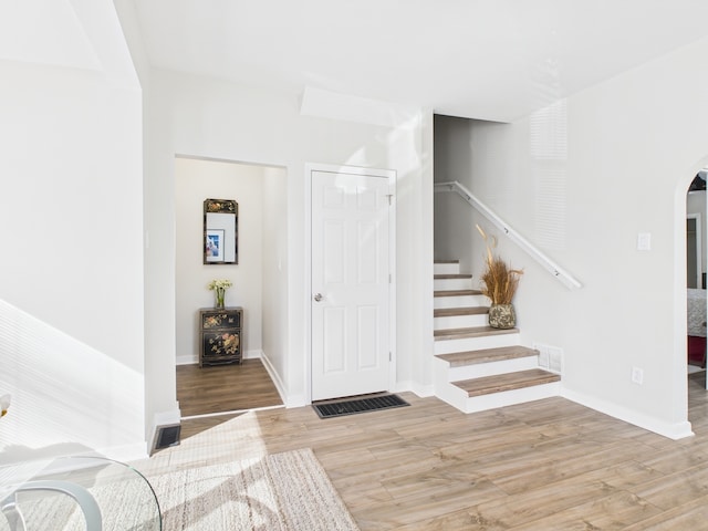 staircase featuring visible vents, arched walkways, baseboards, and wood finished floors