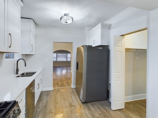 kitchen with stainless steel appliances, sink, white cabinets, and light wood-type flooring