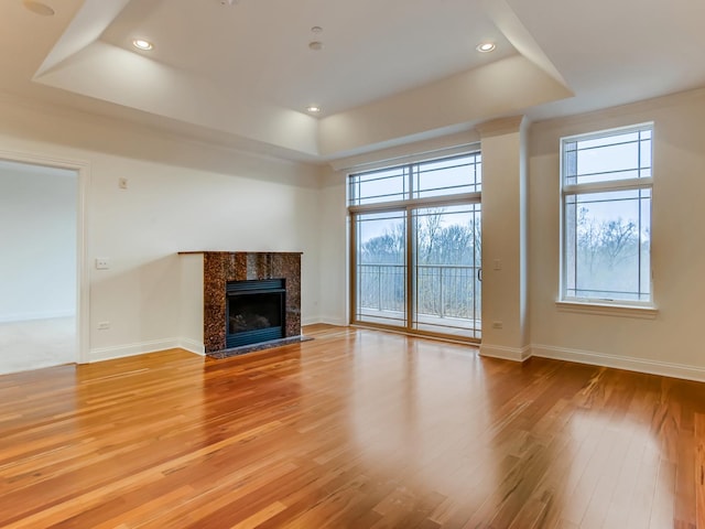 unfurnished living room with a tray ceiling, a tiled fireplace, and light wood-type flooring