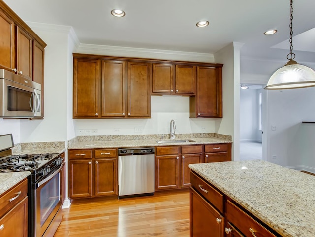 kitchen with sink, crown molding, appliances with stainless steel finishes, decorative light fixtures, and light wood-type flooring