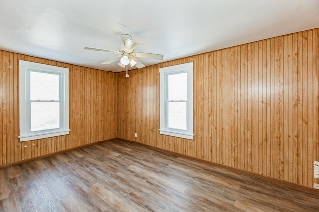 spare room with wood-type flooring, wooden walls, and ceiling fan