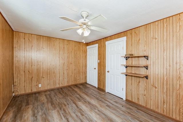 unfurnished room with hardwood / wood-style floors, ceiling fan, and wood walls