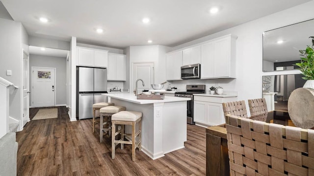 kitchen with a kitchen island with sink, stainless steel appliances, dark hardwood / wood-style floors, a kitchen breakfast bar, and white cabinets