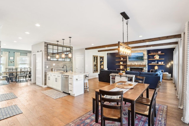 dining room with beamed ceiling, sink, a fireplace, and light wood-type flooring