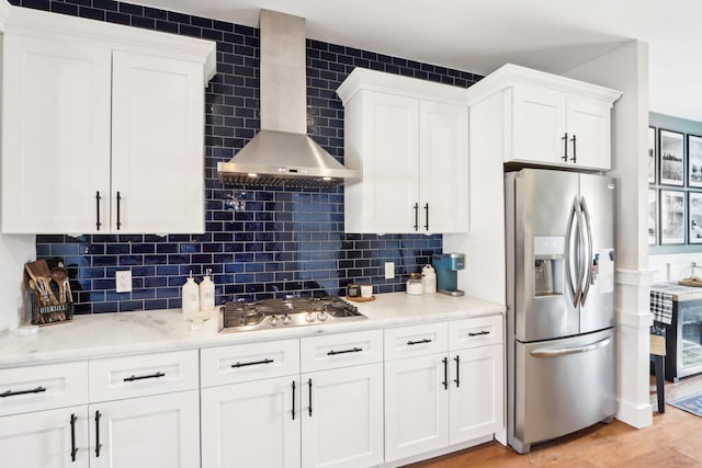 kitchen featuring stainless steel appliances, light hardwood / wood-style floors, white cabinets, decorative backsplash, and wall chimney exhaust hood