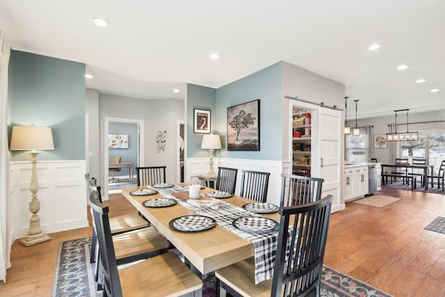 dining area with a wainscoted wall, light wood finished floors, a barn door, and recessed lighting