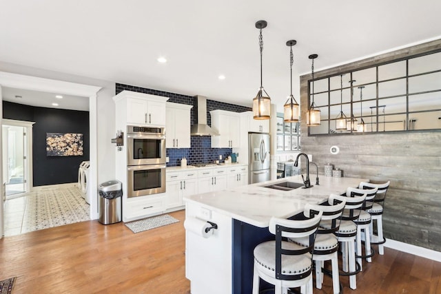 kitchen with stainless steel appliances, sink, wall chimney range hood, and white cabinets