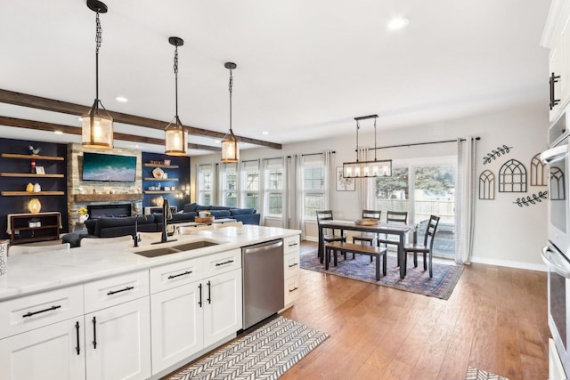 kitchen featuring wood finished floors, a sink, white cabinetry, appliances with stainless steel finishes, and beam ceiling