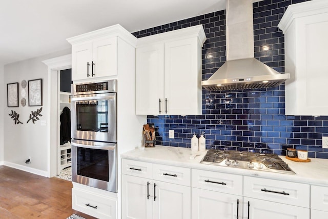 kitchen featuring wall chimney range hood, white cabinetry, stainless steel appliances, and backsplash