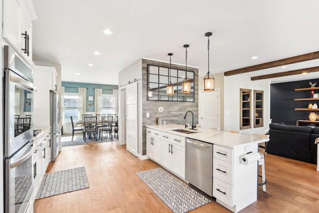 kitchen featuring light wood finished floors, stainless steel appliances, tasteful backsplash, light countertops, and a sink