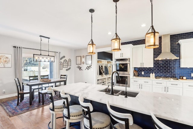 kitchen with a breakfast bar area, tasteful backsplash, appliances with stainless steel finishes, a sink, and wall chimney range hood