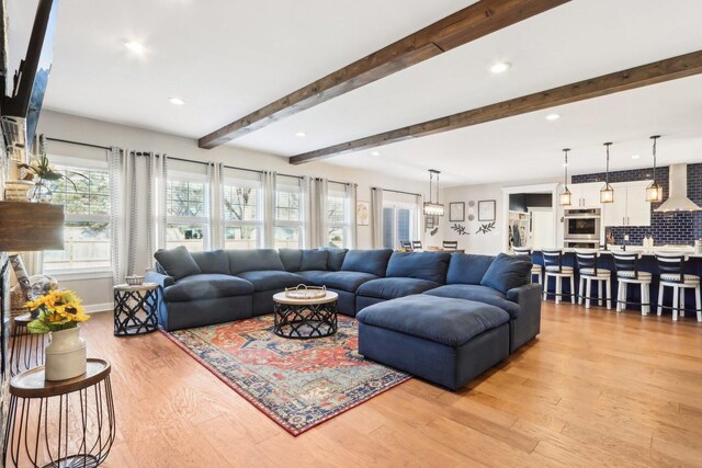 living room featuring beam ceiling, a stone fireplace, and wood-type flooring