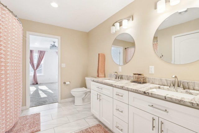 bathroom featuring baseboards, a sink, toilet, and double vanity