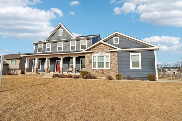 craftsman-style home with stone siding, covered porch, fence, and a front lawn