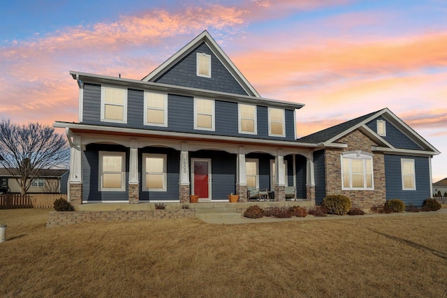 view of front of house with stone siding, covered porch, and a lawn