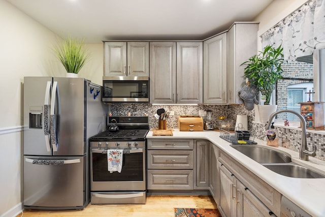 kitchen featuring sink, light hardwood / wood-style flooring, gray cabinets, appliances with stainless steel finishes, and backsplash