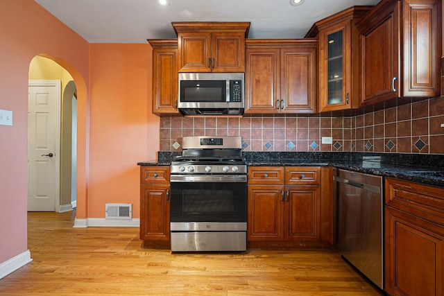 kitchen featuring dark stone countertops, decorative backsplash, light wood-type flooring, and appliances with stainless steel finishes