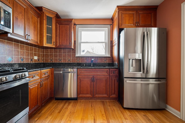 kitchen with sink, light hardwood / wood-style flooring, backsplash, stainless steel appliances, and dark stone counters