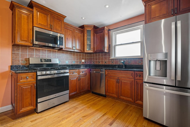 kitchen featuring sink, dark stone countertops, appliances with stainless steel finishes, light hardwood / wood-style floors, and backsplash