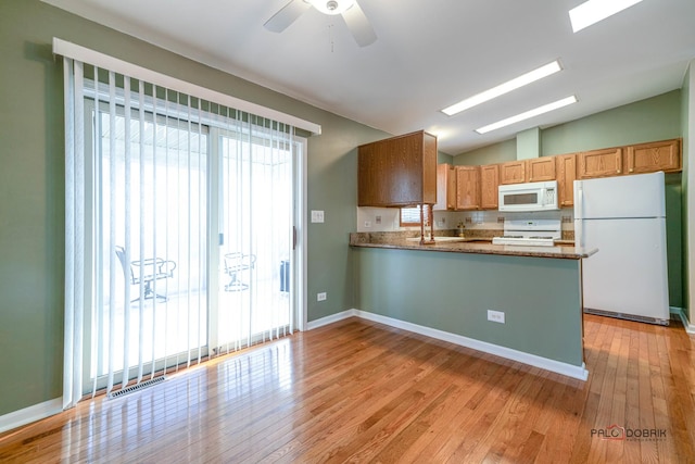 kitchen with stone countertops, vaulted ceiling with skylight, white appliances, kitchen peninsula, and light wood-type flooring