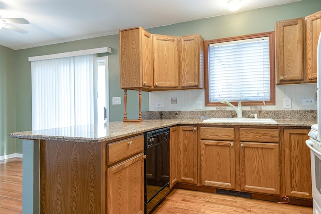 kitchen with sink, black dishwasher, light stone counters, light hardwood / wood-style floors, and decorative backsplash