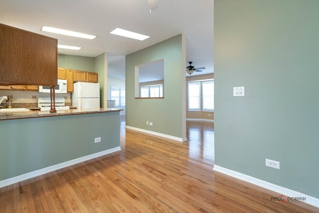 kitchen with sink, light stone counters, light hardwood / wood-style flooring, ceiling fan, and white appliances