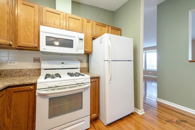 kitchen featuring light stone countertops, light hardwood / wood-style floors, white appliances, and decorative backsplash