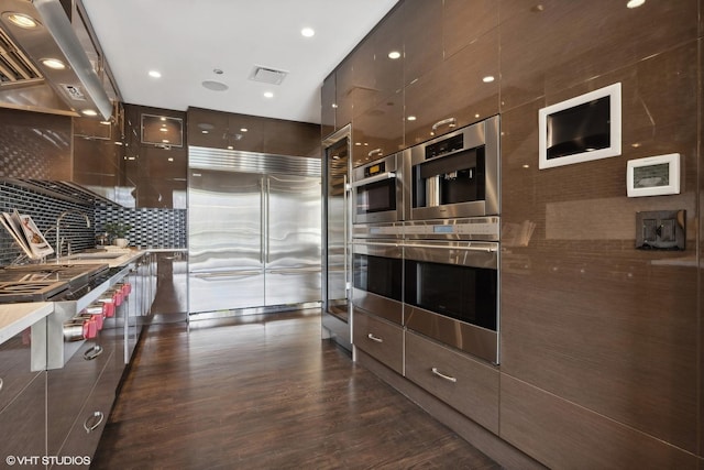 kitchen with sink, stainless steel appliances, tasteful backsplash, dark brown cabinetry, and island exhaust hood