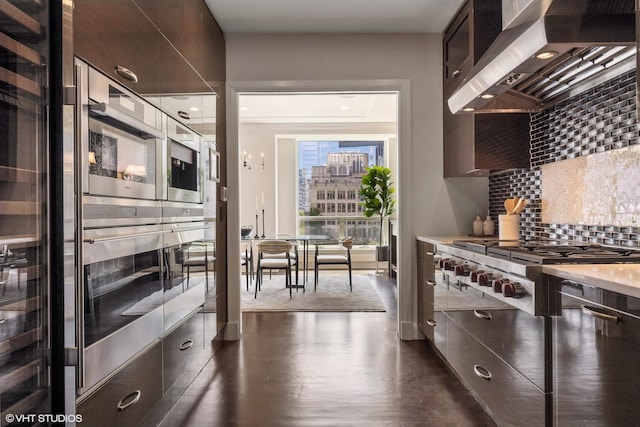 kitchen featuring wall chimney exhaust hood, stainless steel gas cooktop, tasteful backsplash, an inviting chandelier, and dark hardwood / wood-style flooring