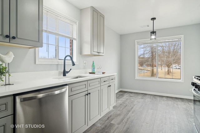 kitchen with sink, gray cabinetry, hanging light fixtures, stainless steel dishwasher, and light wood-type flooring