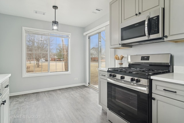 kitchen with gray cabinetry, decorative light fixtures, stainless steel appliances, and light wood-type flooring