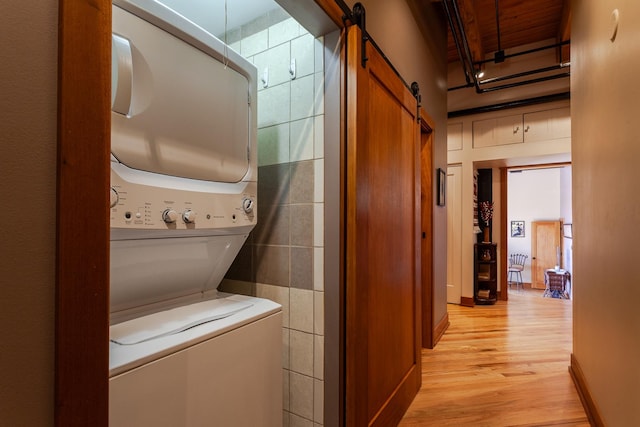 clothes washing area with stacked washer / dryer, a barn door, tile walls, and light hardwood / wood-style floors