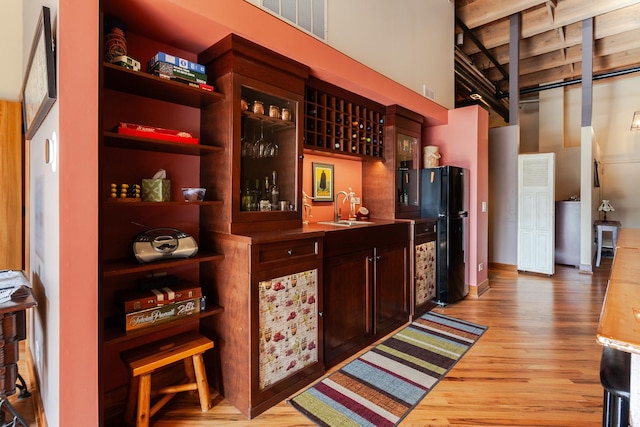 bar with sink, black refrigerator, light wood-type flooring, and a towering ceiling