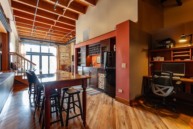 dining space with a towering ceiling, wet bar, beamed ceiling, and light wood-type flooring