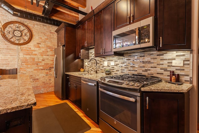 kitchen featuring sink, appliances with stainless steel finishes, backsplash, light stone countertops, and brick wall