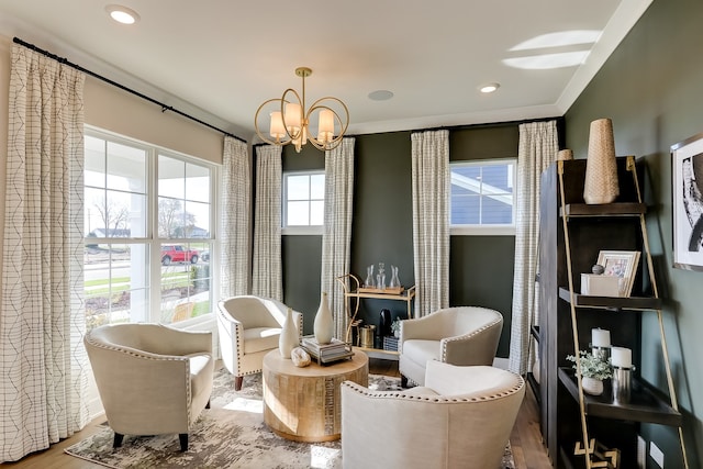 living area with an inviting chandelier, hardwood / wood-style flooring, ornamental molding, and a healthy amount of sunlight