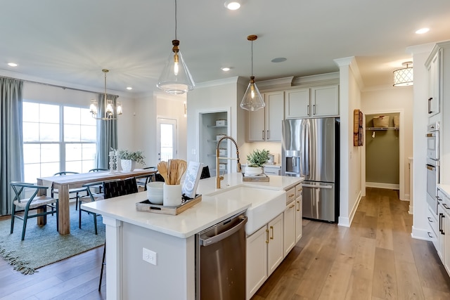 kitchen featuring sink, hanging light fixtures, light hardwood / wood-style flooring, appliances with stainless steel finishes, and a kitchen island with sink