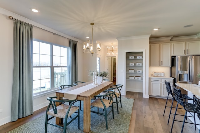 dining area with an inviting chandelier, ornamental molding, light hardwood / wood-style floors, and built in features