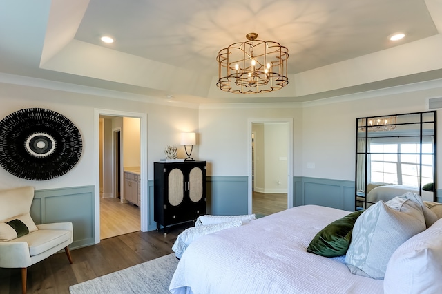 bedroom with connected bathroom, dark hardwood / wood-style flooring, ornamental molding, a notable chandelier, and a raised ceiling