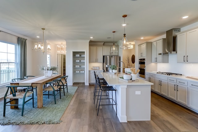 kitchen with a kitchen island with sink, wall chimney range hood, decorative light fixtures, and stainless steel appliances