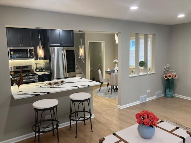 kitchen featuring a breakfast bar, appliances with stainless steel finishes, light hardwood / wood-style floors, decorative backsplash, and kitchen peninsula