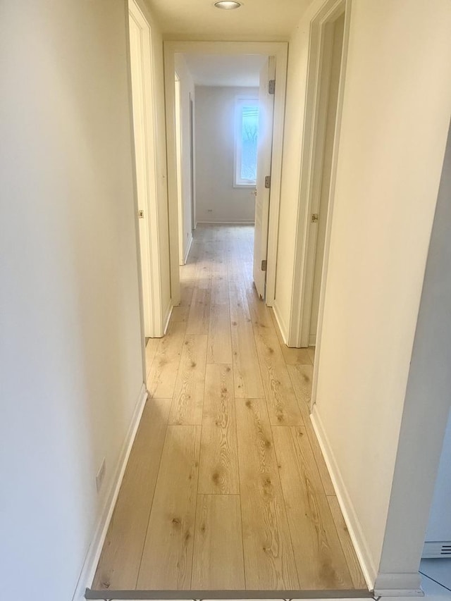 corridor featuring light wood-style flooring and baseboards