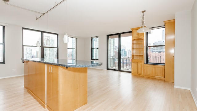 kitchen with dark stone countertops, a wall of windows, hanging light fixtures, a center island, and light hardwood / wood-style floors