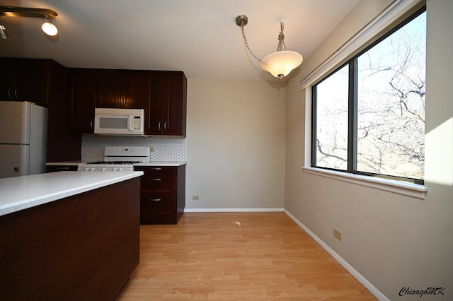 kitchen with tasteful backsplash, light hardwood / wood-style flooring, white appliances, and decorative light fixtures