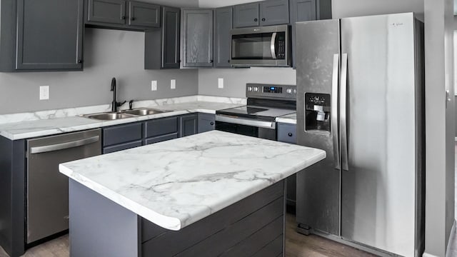 kitchen featuring appliances with stainless steel finishes, gray cabinets, a center island, and sink