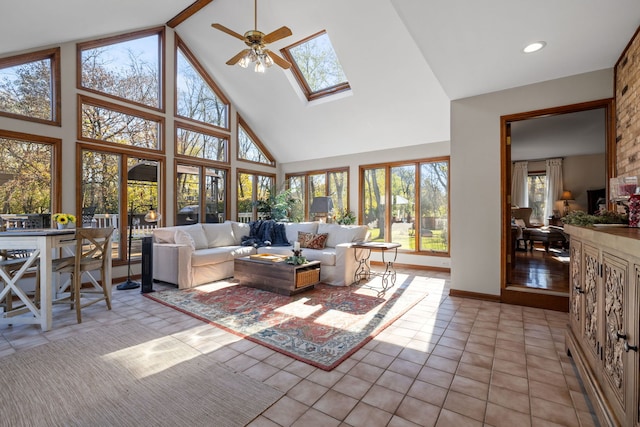 living room with ceiling fan, a skylight, high vaulted ceiling, and light tile patterned floors